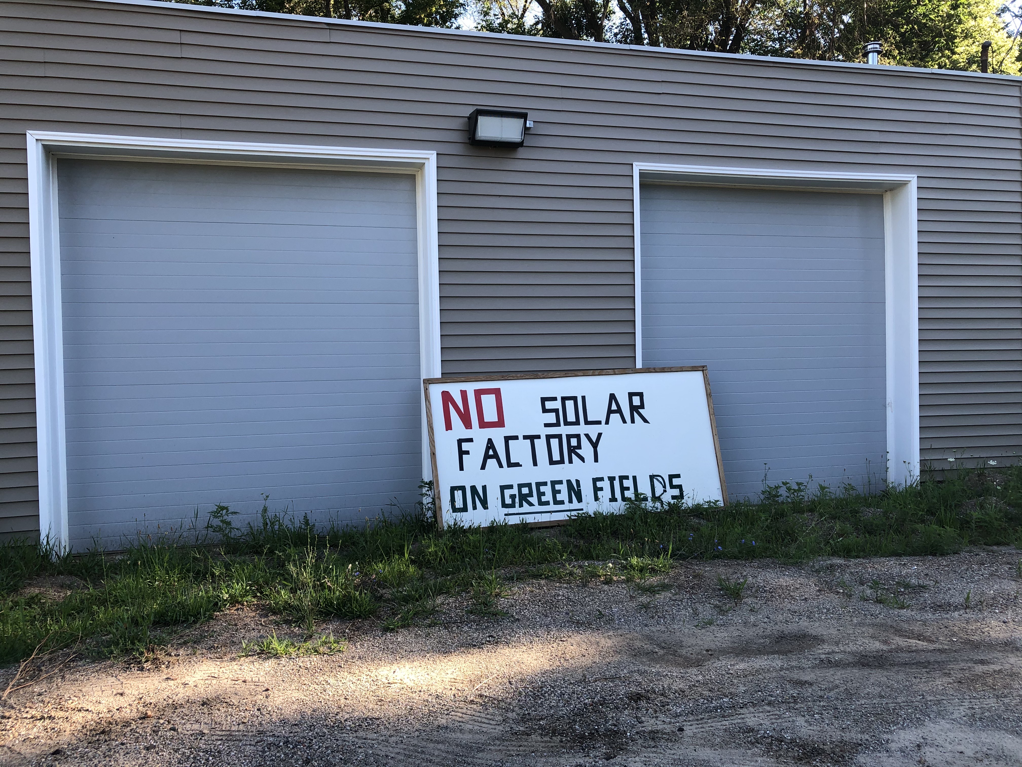 一个米黄色的建筑旁边，有一个写着“绿色土地上没有太阳能工厂”的字母院子标志。
