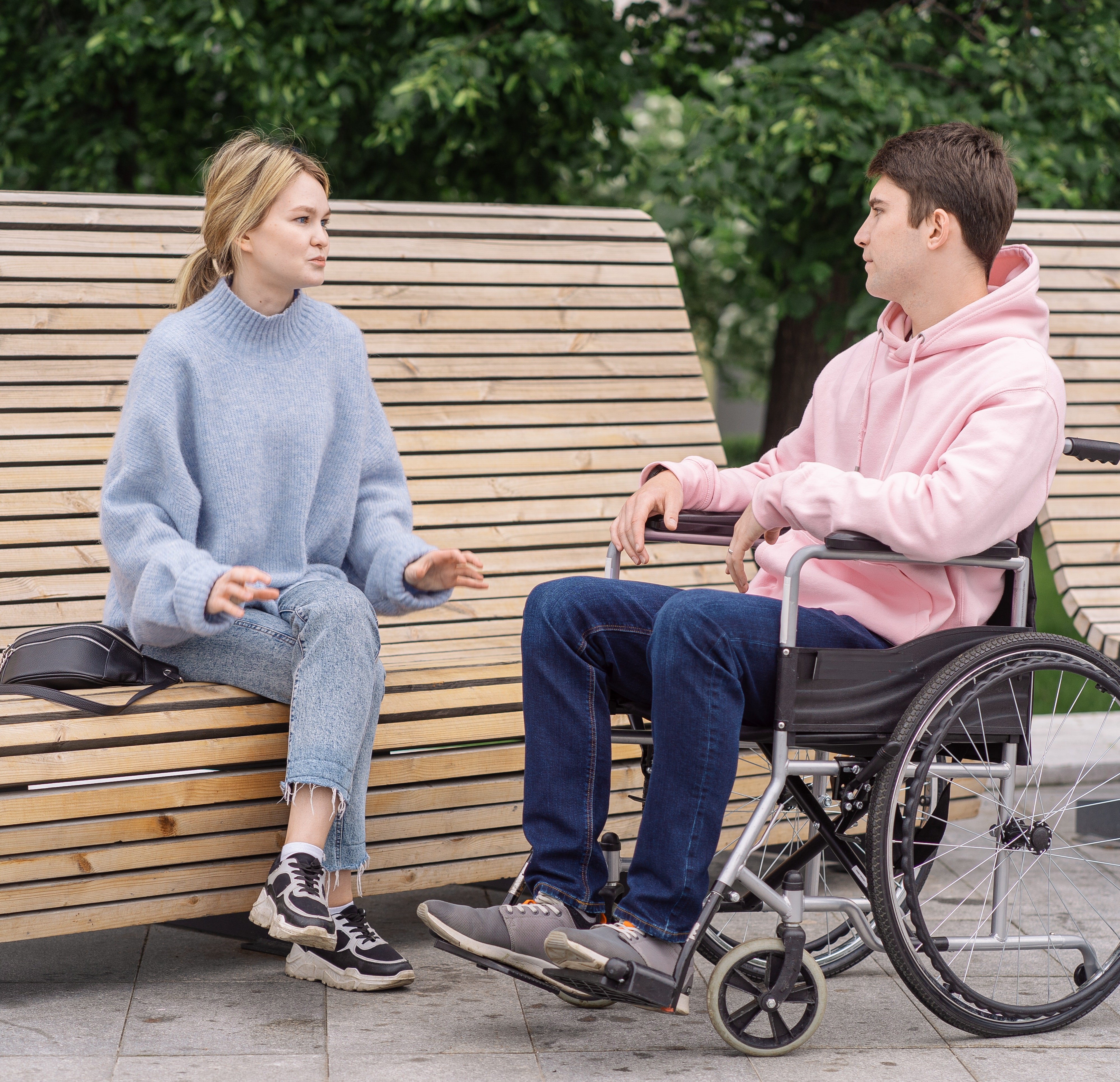 坐在轮椅上的年轻男子和坐在公园长凳上的年轻女子交谈。