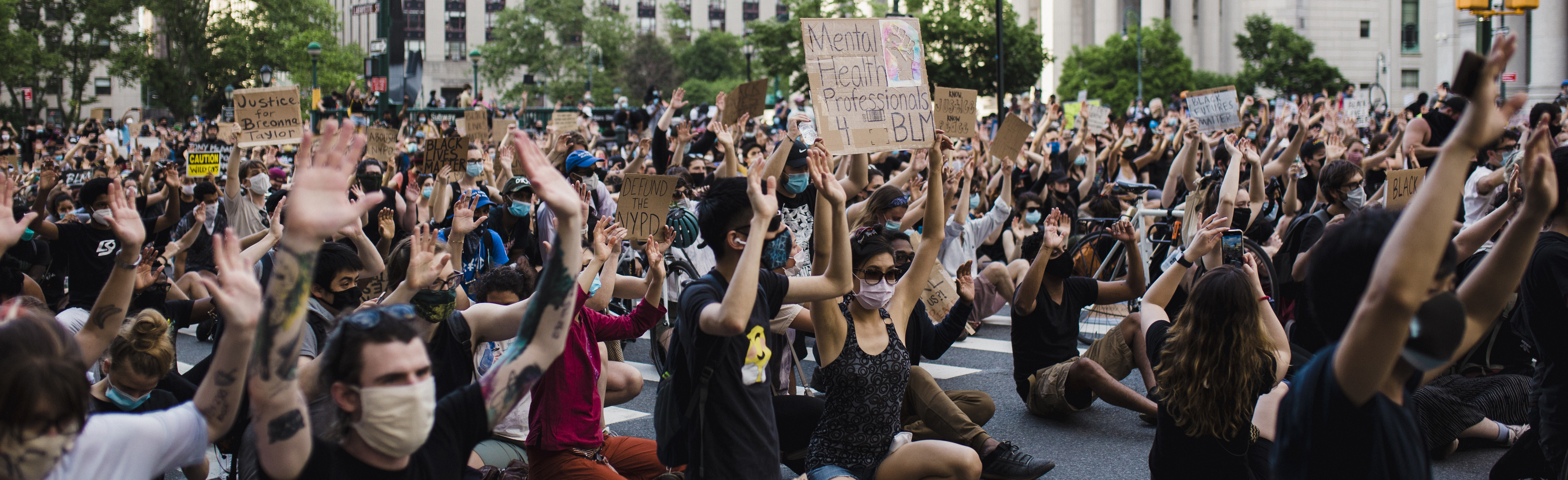 一群抗议者戴着口罩，举着标语，跪在地上。